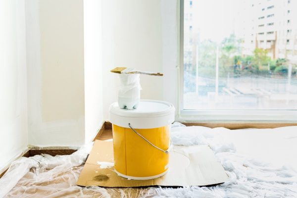 Brush with white paint on a bucket of plastic paint without odors, ecological.