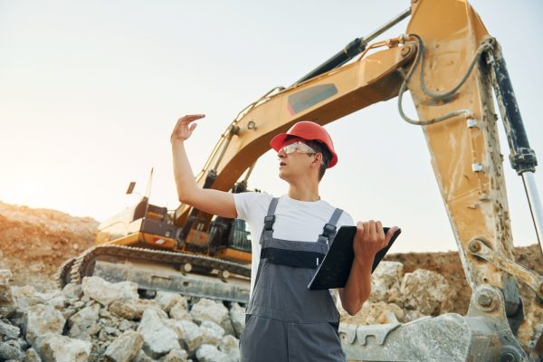 Looking at distant object. Worker in professional uniform is on the borrow pit at daytime.