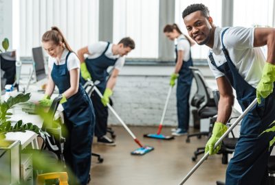 selective focus of smiling multicultural team of cleaners washing floor with mops in office